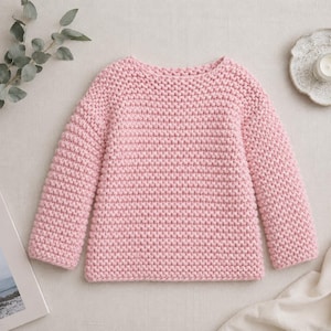 May include: A long-sleeved sweater in a soft pastel pink hue, crafted with a chunky knit texture. The garment features a simple crew neckline and a straight hem, showcasing a consistent, dense stitch pattern throughout the entire piece.