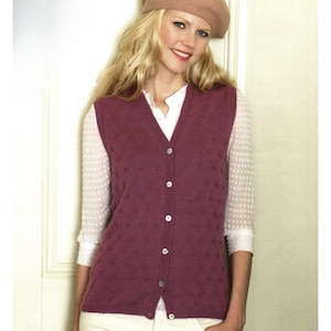 May include: A burgundy knitted vest with a V-neck and button-down front. The vest features a subtle textured pattern and is worn over a white blouse. A light brown beret completes the outfit, creating a classic, layered look.