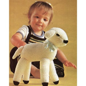 May include: A handmade, white knitted lamb toy with black hooves and a light blue ribbon around its neck. The lamb is a soft, plush toy, perfect for a child. The lamb is a classic, timeless toy.