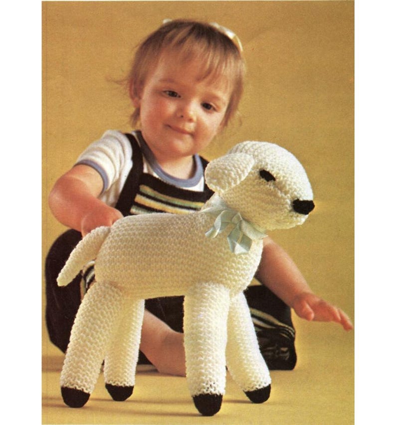 May include: A handmade, white knitted lamb toy with black hooves and a light blue ribbon around its neck. The lamb is a soft, plush toy, perfect for a child. The lamb is a classic, timeless toy.