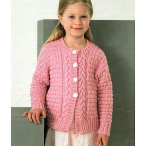 Könnte beinhalten: Ein hellrosa Strickcardigan mit rundem Ausschnitt und weißen Knöpfen. Der Pullover hat ein Zopfmuster auf der Vorderseite und an den Ärmeln. Der Cardigan wird von einer jungen Person getragen.