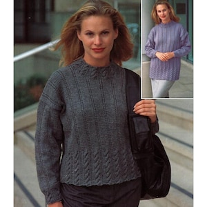 Könnte beinhalten: Eine Frau trägt einen grauen Strickpullover mit Rippenmuster und hohem Ausschnitt. Der Pullover hat ein strukturiertes Muster und lange Ärmel. Ein kleineres Bild zeigt einen ähnlichen Pullover in Lavendel.