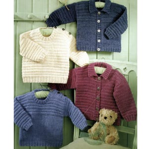 Könnte beinhalten: Vier gestrickte Kinderpullover in Creme, Marineblau und Burgunderrot. Zwei sind Rundhalspullover und zwei sind Cardigans zum Knöpfen. Ein kleiner Teddybär sitzt vor einem der Cardigans auf einem Stuhl.