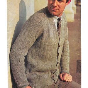 May include: A light brown cardigan sweater with a ribbed knit design. The sweater has a V-neck, long sleeves, and brown buttons. The person is wearing a patterned tie and a light-colored shirt.