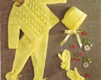 May include: A complete baby outfit in a soft yellow knit. The set includes a sweater, footed pants, a bonnet with a ribbon tie, and matching mittens. The sweater has a decorative cable knit pattern. The outfit is displayed on a wooden hanger.