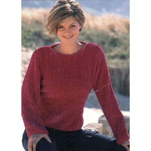 Puede incluir: Un suéter de color burdeos con textura acanalada. La parte superior de manga larga tiene cuello redondo y se usa con pantalones azul oscuro. El suéter parece estar hecho de un material suave y afelpado.