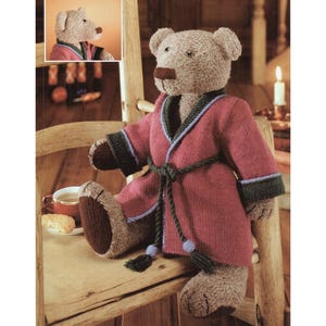 May include: A knitted teddy bear wearing a red dressing gown with dark green and blue detailing, and a matching belt. The bear is seated on a wooden chair, with a cup of tea and a biscuit nearby. A smaller image of the bear is in the top left.