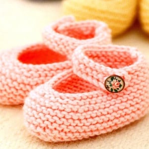 May include: A pair of pink knitted baby shoes with a floral button on one shoe.