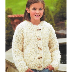 May include: A cream-colored, textured knit cardigan with wooden toggle closures. The sweater has a round neckline and long sleeves. The cardigan is worn over blue jeans. The overall style is casual and comfortable.