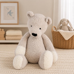 May include: A large, plush teddy bear with a light gray body and white accents on its paws. The bear has a black nose and small black eyes. A woven basket with a stuffed bunny is in the background.