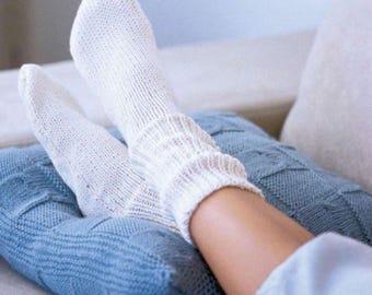 May include: A pair of white knitted socks with ribbed cuffs. The socks are worn on a person's legs, resting on a blue knitted blanket. The socks appear soft and comfortable, suggesting a cozy, relaxed setting.