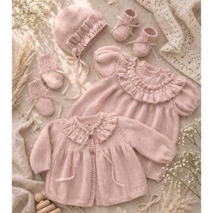 May include: A collection of baby clothing in a soft pink hue. The set includes a bonnet, two pairs of socks, two pairs of booties, and two sweaters. The sweaters have a ruffled collar and ribbon ties. The items are made of a knitted material.
