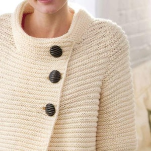 Pu&ograve; includere: Un cardigan di maglia color crema con chiusura leggermente asimmetrica e tre bottoni marroni scuri. Il cardigan ha un collo alto e maniche corte.