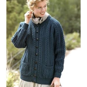 May include: A dark teal cardigan with a cable knit design, featuring a button-up front and two front pockets. The sweater has a round neckline and long sleeves. The woman is wearing a scarf around her neck.