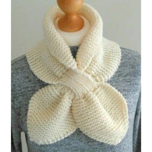 May include: A cream-coloured, hand-knitted scarf with a distinctive petal design. The scarf is displayed on a mannequin, highlighting its textured knit and soft, neutral colour. A cosy accessory.