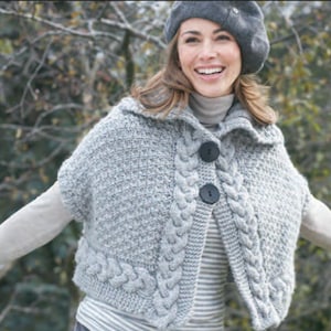 May include: A gray knitted cape with a cable knit design and two large black buttons. The cape has a collar and short sleeves. A gray beret is also visible.
