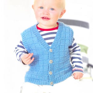 May include: A light blue knitted baby vest with a textured, square pattern. The vest has a V-neck and is fastened with four round, light-colored buttons. The baby is wearing a striped shirt underneath.