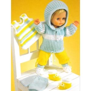 May include: A doll wearing a light blue and white hooded sweater, yellow pants, and white shoes. Additional knitted clothing includes a striped vest and light blue shorts. The doll is posed on a white chair.