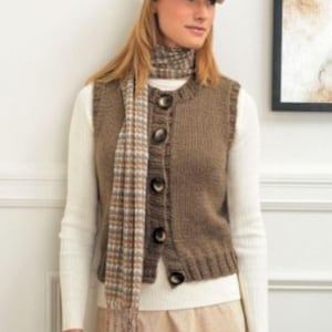 Puede incluir: Un chaleco de punto marrón con botones grandes y oscuros. El chaleco se lleva sobre una camisa blanca de manga larga y se combina con una bufanda a cuadros. El conjunto se completa con un sombrero a juego. El estilo general es informal y adecuado para el clima fresco.