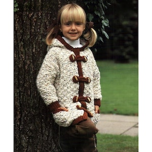 Peut inclure: Une veste tricotée à capuche de couleur crème avec des fermetures à bascule et des bordures marron. La veste présente un motif texturé et est portée par une jeune personne. La veste a un aspect fait main et confortable, adaptée au temps frais.