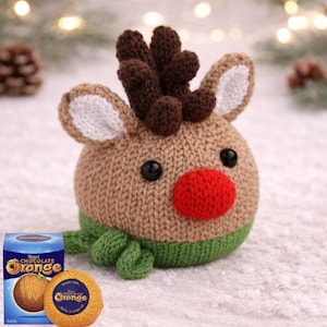 Könnte beinhalten: Ein handgefertigtes gestricktes Rentierspielzeug mit roter Nase, braunem Geweih und schwarzen Augen. Das Rentier hat einen grünen Schal und weißspitzige Ohren. Eine Schachtel Terry's Chocolate Orange und eine Orangen-Schokolade sind im Bild.