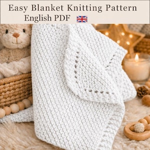 May include: A white knitted blanket with a textured stitch pattern and a decorative border. The text at the top reads Easy Blanket Knitting Pattern English PDF. A light brown teddy bear and wooden beads are visible in the composition.