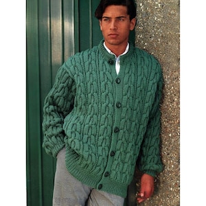 Può includere: Un cardigan verde con bottoni e un design a maglia a treccia strutturata. Il maglione ha un collo alto e maniche lunghe. I bottoni sono scuri e il cardigan è indossato sopra una camicia bianca.