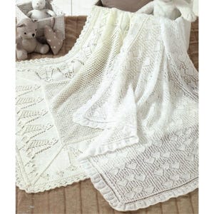 Puede incluir: Dos mantas blancas para bebé, intrincadamente tejidas. Una manta presenta un detallado patrón de hojas, mientras que la otra muestra un diseño en forma de corazón. Las mantas están dobladas y drapeadas, mostrando el delicado calado. Un osito de peluche y una cesta están en el fondo.