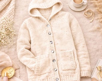 May include: Cream-colored hooded cardigan sweater with a button-up front and two front pockets. The sweater is made of a chunky knit material and has a relaxed fit. The buttons are silver. The sweater is displayed on a soft, neutral-toned surface.