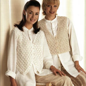Puede incluir: Dos mujeres con camisas blancas y chalecos de crochet color crema. Los chalecos tienen un diseño de tejido abierto en forma de diamante y cuello en V. Se abrochan con pequeños botones redondos. Primer plano de los chalecos.
