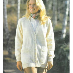 Op de afbeelding: Crèmekleurig vest met knopen en twee voorzakken. De trui heeft een V-hals en lange mouwen. De persoon draagt een wit overhemd met kraag en een sjaal met patroon.