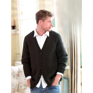 May include: Dark green cardigan sweater with a V-neck and button closure. The sweater is worn over a white collared shirt and blue jeans. The cardigan has long sleeves and a ribbed hem and cuffs. The person is standing near a window.