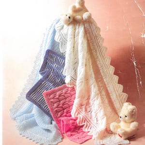 May include: A collection of knitted baby blankets in various colors, including white, light blue, lavender, and pink. Each blanket features a unique pattern and decorative edging. A small teddy bear is placed near the blankets.