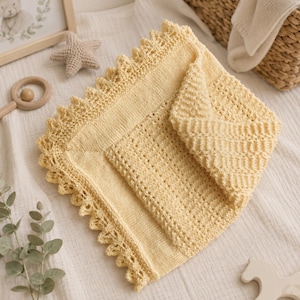 May include: A soft, pale yellow knitted blanket featuring a delicate, intricate lace-like border with a scalloped edge. The center of the blanket displays a smooth, stockinette stitch texture, while the surrounding panel showcases a textured, ribbed pattern.