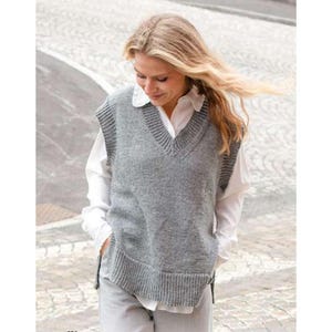 Puede incluir: Un chaleco gris con cuello en V y detalles acanalados en el cuello, las sisas y el dobladillo. Se lleva sobre una camisa blanca con cuello. El estilo es informal y cómodo, adecuado para combinar.