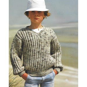 May include: A ribbed knit sweater in shades of gray and brown, featuring a V-neck design. The sweater is worn with blue jeans and a white bucket hat. The overall style suggests a casual, comfortable aesthetic, suitable for cooler weather.