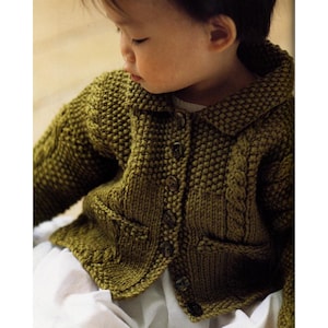 May include: A close-up of a knitted olive green cardigan with a collar, two front pockets, and wooden buttons. The cardigan features a textured knit pattern and cable knit detailing on the sleeves. The garment is worn over a white garment.