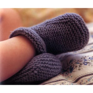 May include: A close-up of a knitted, purple sock and leg warmer set. The leg warmer is wrapped around the leg, and the sock is on the foot. The items are made of a thick, textured yarn, suggesting warmth and comfort. The background is a floral patterned fabric.