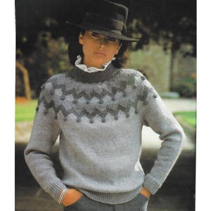 May include: A light gray sweater with a patterned yoke and long sleeves. The yoke features a zig-zag design in darker gray, with small, round embellishments. The sweater has a ribbed collar and cuffs.