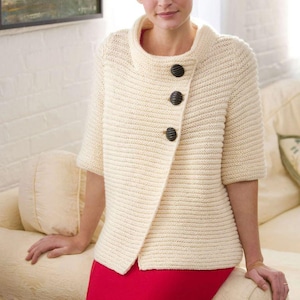 Peut inclure: Un cardigan blanc en tricot avec un col montant et trois boutons noirs. Le cardigan a une coupe légèrement asymétrique et est réalisé avec un point texturé.