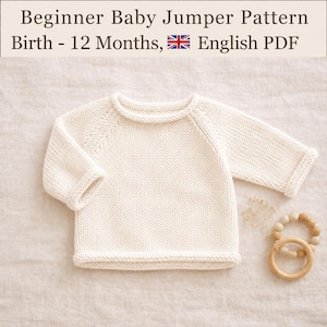 Puede incluir: Un suéter de bebé tejido en color crema con mangas largas y cuello redondo. El texto en la parte superior dice: Beginner Baby Jumper Pattern Birth - 12 Months, English PDF. Un pequeño juguete de anillo de madera con cuentas claras está al lado.