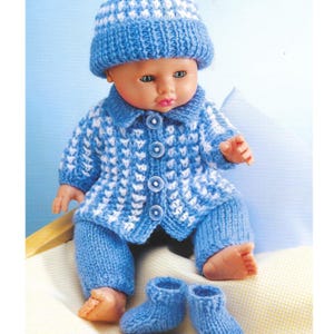 Op de afbeelding: Een pop gekleed in een blauw en wit gebreid outfit, bestaande uit een muts, jasje, broek en booties. Het jasje heeft drie knopen. De outfit is lichtblauw met een wit patroon.