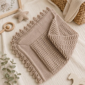 May include: A square, light beige knitted blanket featuring a central panel with a textured, open-work stitch pattern, surrounded by a smooth stockinette border and finished with a delicate, scalloped lace edge along all four sides.
