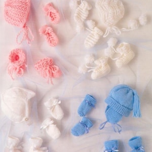 May include: A set of knitted baby items in pink, white, and blue. The set includes a hat, booties, and mittens. The items are made with soft yarn and are perfect for a newborn baby.