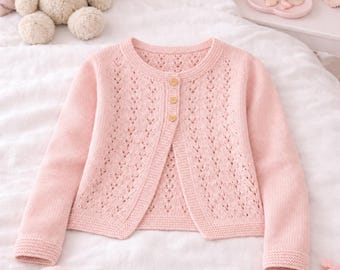 May include: A light pink, open-front cardigan with a delicate, openwork design. The long-sleeved sweater features a round neckline and is fastened with three wooden buttons. The knitted garment is displayed on a white surface.