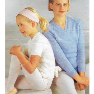 May include: Two young people wearing knitted tops and leggings. One person is wearing a white short-sleeved top with a bow in the back and white leggings. The other person is wearing a light blue wrap-style sweater and white leggings.