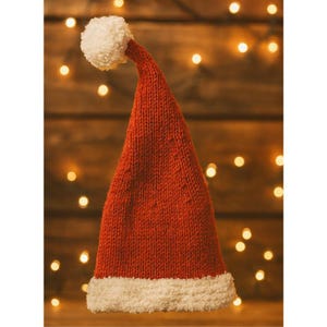 Könnte beinhalten: Ein roter gestrickter Weihnachtsmannhut mit weißem, flauschigem Rand und Bommel. Der Hut besteht aus einem strukturierten, warmen Material, perfekt für die Weihnachtszeit. Der Hintergrund zeigt weiche, unscharfe Lichter und schafft eine festliche Atmosphäre.