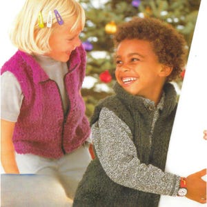 May include: Two children wearing knitted vests, one in a vibrant fuchsia and the other in a dark green. The fuchsia vest has a zipper, while the green vest has a button closure. Both children are smiling, suggesting a joyful moment. The background is a blurred Christmas tree.