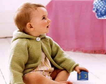 Puede incluir: Un bebé con una rebeca con capucha de punto verde claro con un botón blanco grande. El bebé sostiene un bloque azul con la letra "C". El bebé lleva un body a rayas. La rebeca es una prenda suave y cómoda.