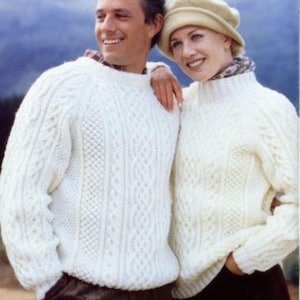 Può includere: Due persone con maglioni color crema a trecce abbinati. I maglioni hanno uno scollo tondo e un motivo strutturato. La donna indossa anche un basco beige e una sciarpa fantasia. Lo sfondo è una scena sfocata all'aperto.